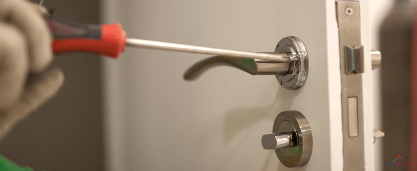 A locksmith fixes a door lock using a screwdriver.